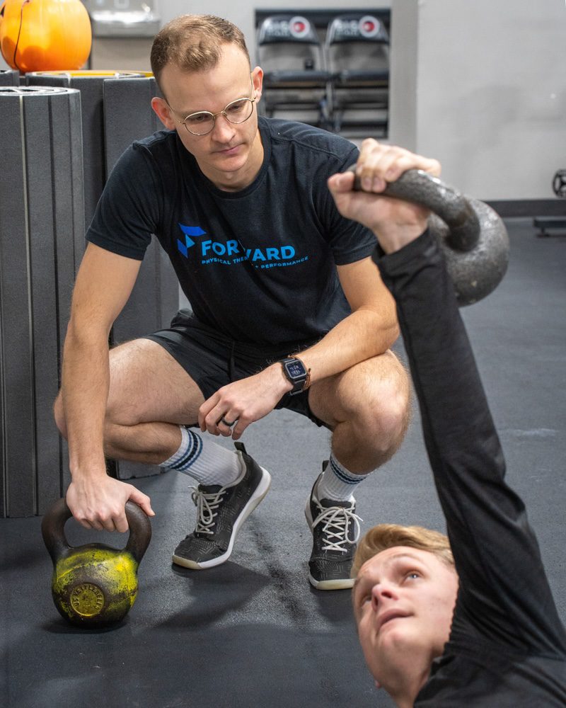 a boy doing kettlebell lifts with his left arm as a physical therapist observes